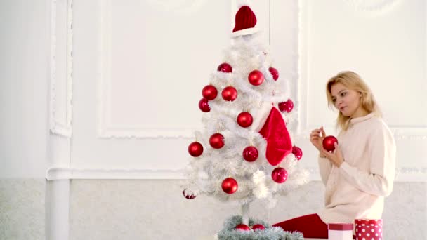 Preparación navideña. Mujer rubia sosteniendo bola roja de Navidad en el árbol de Navidad blanco. Decoraciones de Navidad . — Vídeos de Stock