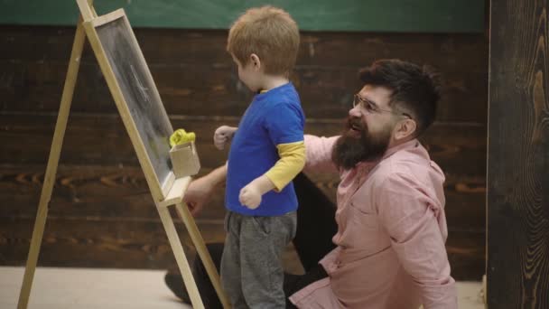 Dibujo del alumno en pizarra. El profesor controla el proceso de aprendizaje. Padre enseñando hijo. Alumno con profesor en la escuela. Vista lateral padre e hijo aprenden aritmética. Papá explicando ecuación a chico lindo . — Vídeos de Stock