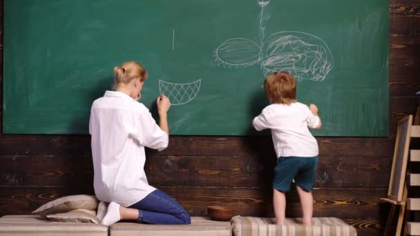 Moeder en haar zoon tekenen met krijt op school op Green Blackboard, achteraanzicht. Vrouw en jongen gelijkspel. Terug naar school. Leerconcept. Kwekerij leraar en kind jongen schilderij foto op schoolbord. — Stockvideo