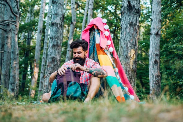 Acogedora tienda de juegos para hombre en el parque forestal. Senderismo y concepto de recreación al aire libre con viajes de camping plano. Hombre barbudo guapo divirtiéndose en aventura Park . — Foto de Stock