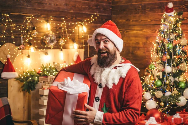 O Pai Natal está a guardar presentes. Homem Hipster, o Pai Natal barbudo celebra o Dia de Acção de Graças e o Natal. Hipster em chapéu vermelho Santa segurando presente. — Fotografia de Stock