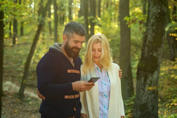 Autumn couple with phone. Happy couple using smart phone. Man typing write message on smart phone in autumn park. Autumnal mood.