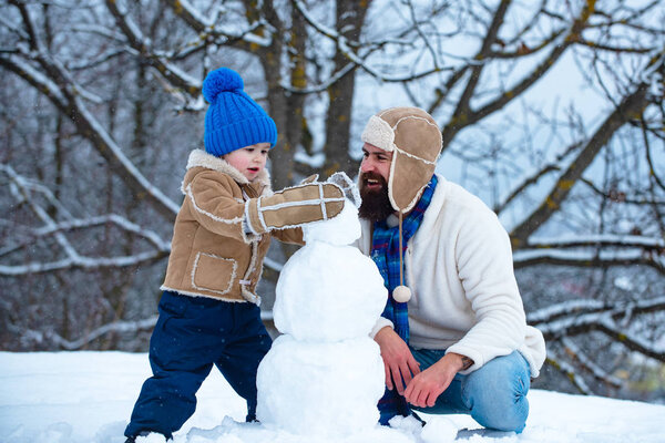 Отец и сын делают снеговика на снегу. Снеговик ручной работы. Рождественские праздники и зимний Новый год с отцом и сыном. Счастливая семейная коса со снеговиком на снежной прогулке.