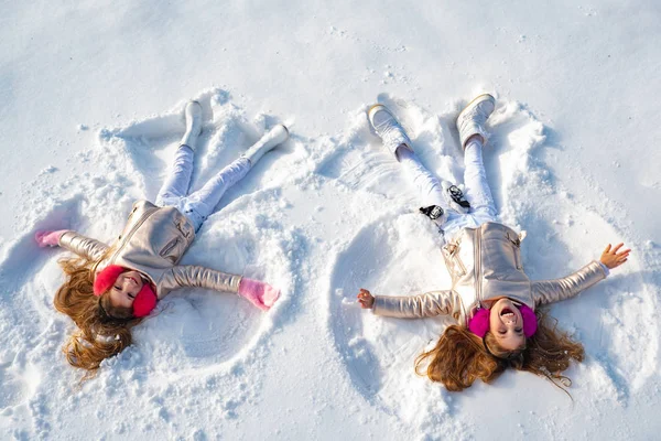 Glad tjej på en snöängelshow. Två små flickor som gör snö ängel medan de ligger på snö. — Stockfoto