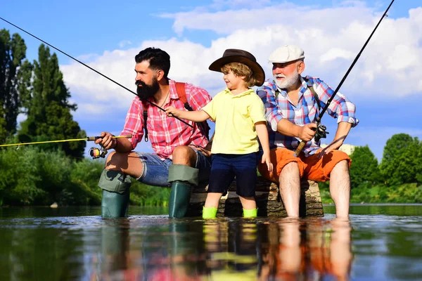 Un uomo che insegna ai bambini a pescare nel fiume. Nonno, padre e ragazzo pescano insieme. Papà e figlio pesca al lago. Weekend estivo. — Foto Stock