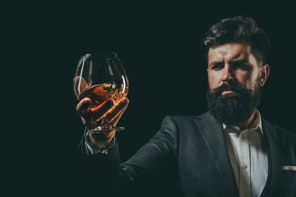 Empresario barbudo en traje elegante con vaso de coñac. Concepto de bebidas de lujo. Hombre Camarero sosteniendo vaso de coñac . — Foto de Stock