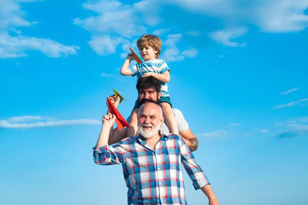 Multi generation. Weekend family play. Men in different ages. Happy child playing with toy paper airplane against summer sky background. Child happy. Father and son playing on blue summer sky.