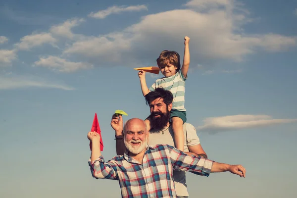 Generación de personas y etapas de crecimiento. Aviador piloto infantil con avión de papel sueña con viajar. Niño con padre y abuelo disfrutando juntos en el parque sobre fondo azul del cielo . — Foto de Stock