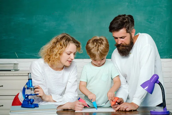 Partnerschaftsmodelle für Schulgemeinschaften. Grundschüler. Glückliches junges Paar, das mit seinem Sohn beim Abschluss steht. Junges Paar hilft seinem Sohn bei den Hausaufgaben. — Stockfoto