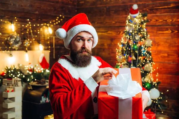 Hombre de Santa sosteniendo regalo. Hipster hombre, barbudo de Santa celebrar el día de Acción de Gracias y la Navidad. Hipster en rojo Santa sombrero celebración presente. —  Fotos de Stock