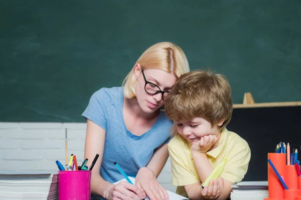 Komik küçük çocuk ve genç kadın öğretmen kara tahta arka plan üzerinde eğleniyor. Okulda ki kadın öğretmen ve okul çocuğu. Büyük çalışma başarısı. — Stok fotoğraf