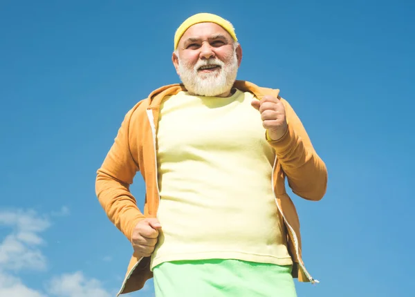 Uomo anziano che pratica sport su sfondo cielo blu. Un anziano che fa jogging. Nonno dell'età dell'oro. Persona anziana di fitness che corre nel parco per buona salute. Vacanze estive e attive . — Foto Stock