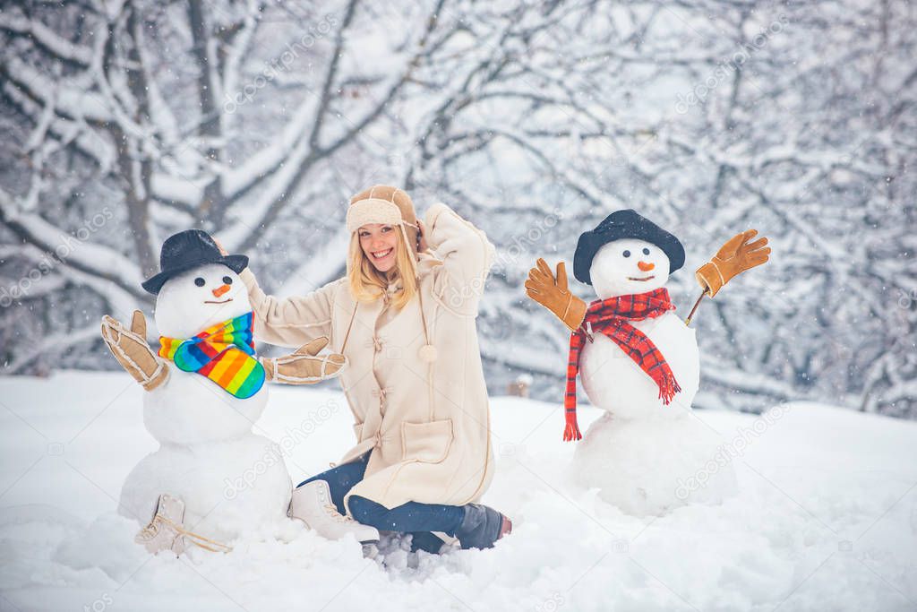 Happy winter time. Winter concept. Snowman and funny girl the friend is standing in winter hat and scarf with red nose.