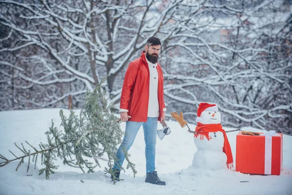 Émotion hivernale. Jeune bûcheron portrait d'hiver. L'homme va couper un sapin de Noël. Homme barbu avec arbre de Noël fraîchement coupé en forêt . — Photo