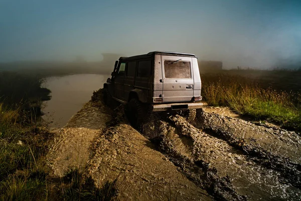 Coche todoterreno en mal camino. Salpicadura de agua en las carreras off-road. Rueda de cerca en un paisaje rural con un camino fangoso . — Foto de Stock