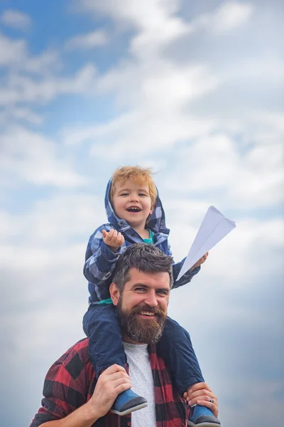 父亲节快乐爸爸和儿子在天空背景下玩耍.小孩坐在他父亲的肩上.梦想的自由-快乐的男孩玩纸飞机。父母之职. — 图库照片