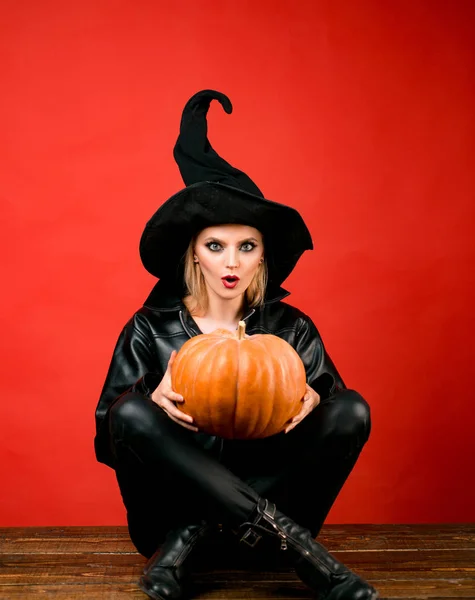 Emotionele jonge vrouwen in halloween kostuums op partij op rode achtergrond met pompoen. Heks poseren met pompoen. — Stockfoto