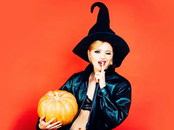 Veselý halloween. Legrační tvář a překvapena žena. ekret Halloween. Emotivní mladé ženy v halloweenových kostýmech na Rudém pozadí s dýní. — Stock fotografie