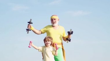 Sağlıklı yetiştirilme. Büyükbaba ve küçük torunu açık havada halter egzersizleri pratik. Spor koçu ve çocuk halterile güç bina.