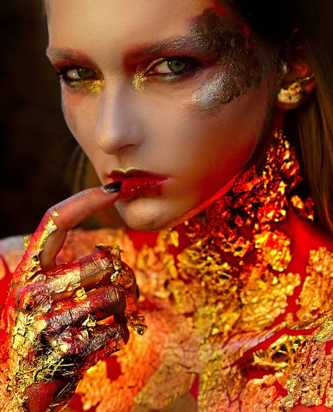 Mujer modelo Halloween de alta moda en brillantes destellos dorados. Belleza ojos dorados labios rojos sangrientos. Bruja Dorada. Belleza moda Halloween chica con Golden make up . — Foto de Stock