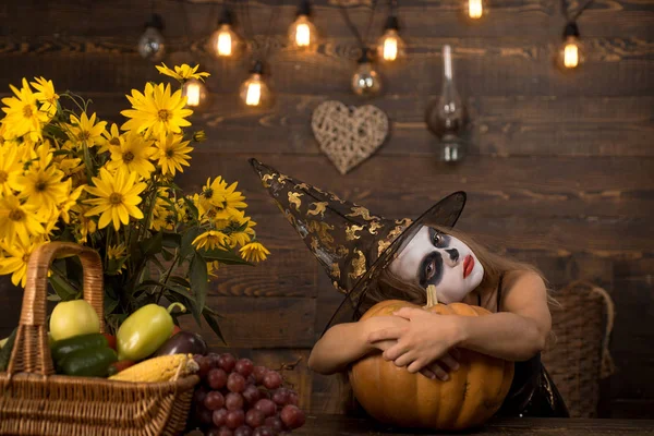 Kleine meisje kind in Halloween kostuum houden oranje pompoen en witte schedel. Kind meisje kind dragen Halloween kostuum met pompoen een oude houten huis. — Stockfoto