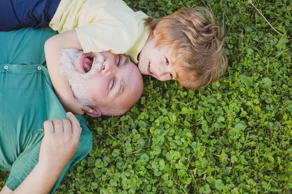 Niño feliz con el abuelo abrazando y abrazando en la hierba verde. El nieto abraza a su abuelo. Feliz abuelo y nieto relajándose juntos . — Foto de Stock