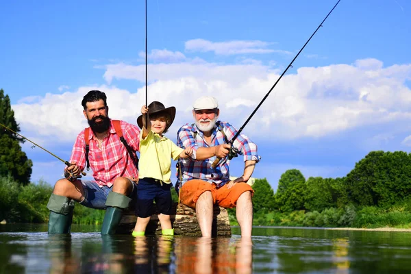 Piccolo ragazzo pesca a mosca su un lago con il padre e il nonno. Giornata estiva. Buon nonno, padre e nipote con canne da pesca sul fiume. Persone felici famiglia hanno pesca e divertimento insieme. — Foto Stock