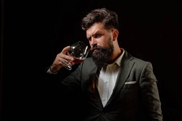 Koncepcja alkoholu. Stylowy elegancki brodaty człowiek Barman trzyma szkło koniakowe. Mężczyzna lub biznesmen pije koniak na czarnym tle. — Zdjęcie stockowe