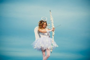 A child in the clothes of an angel on sky background - Valentine concept. The God of Love. Real fairy from magical stories. Lovely girl cupid with bow and arrow is ready to find your love