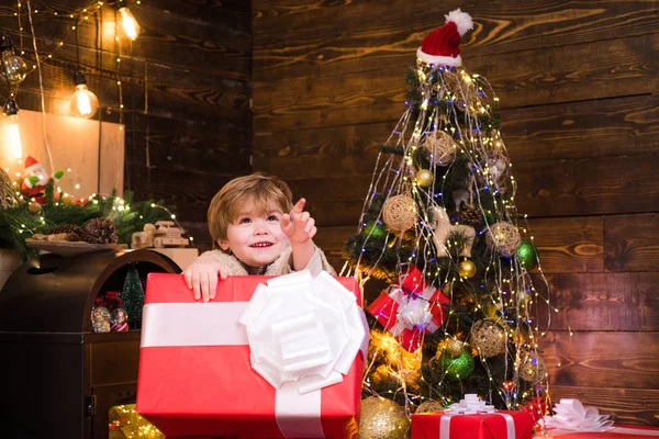 Happy Child med julklapp. Porträtt av Santa Kid med stor röd gåva tittar på kamera. Kid ha kul nära julgran inomhus. — Stockfoto