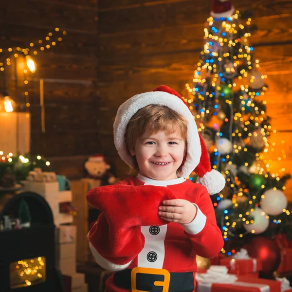 Kindheitsmomente. Kinderfreudiges Gesicht bekam Geschenk in Weihnachtssocke. Kontrollieren Sie den Inhalt von Weihnachtsstrumpf. Freude und Glück. Weihnachtsstrumpfkonzept. Kid boy santa hold weihnachtsgeschenk rote socke — Stockfoto