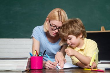 Okula ve mutlu zamanlara geri dönelim. Öğretmen okulda sınıfta ödevlerini çocuklara yardım ediyor. Yetenekli çocuk. Blackboard arka plan - kopyalama alanı.