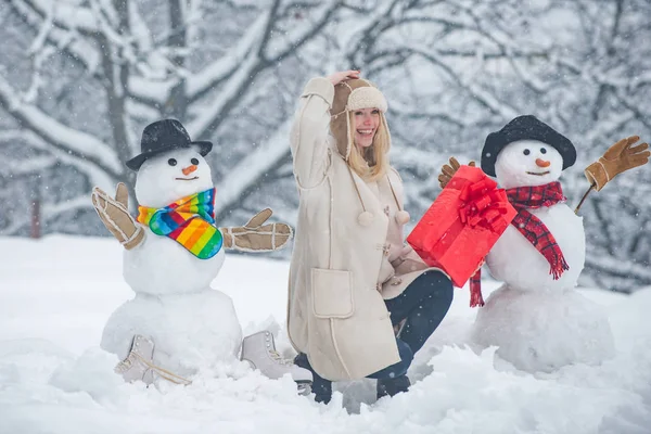 Muñeco de nieve y chica divertida en la nieve. Chica jugando con muñeco de nieve - aislado en el fondo de nieve. Joven bella alegre divirtiéndose con muñeco de nieve en Winter Park . — Foto de Stock