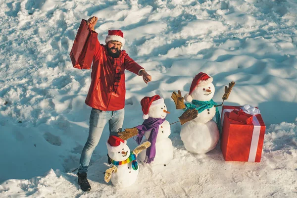 Beau Winter Man avec cadeau et bonhomme de neige dans le parc hivernal givré. Funny Santa homme posant avec boîte cadeau rouge sur le temps d'hiver. Vacances d'hiver et concept de personnes . — Photo