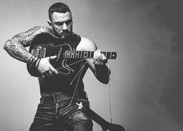 Guitar as weapon. Brutal latino man playing the broken guitar. Hispanic guitarist performing music on electric guitar. Bearded guitarist with string guitar in strong hands, copy space