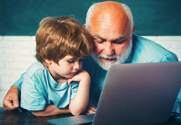 Šťastný dědeček se svým vnukem, aby používal přenosný počítač. Učitel pomáhal svému žákovi na vyučování. Zpět ke škole a vzdělávání. — Stock fotografie