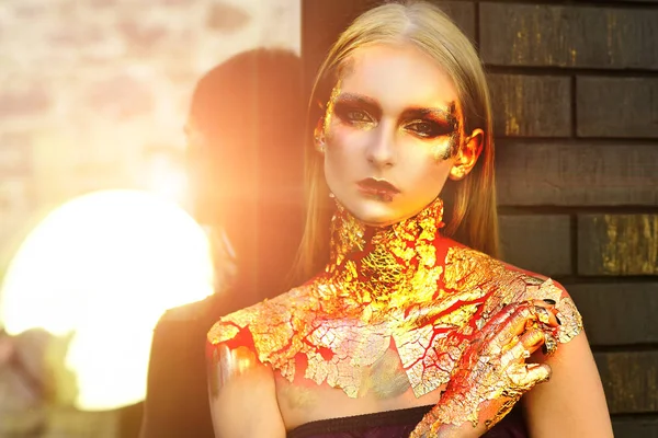 Brillo metálico brillo dorado maquillaje. Mujer vampiro con labios ensangrentados y ojos dorados. Bruja de Halloween con labios rojos sangrientos y piel dorada. Mujer de Halloween oro . — Foto de Stock