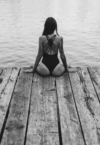 Visão traseira da fêmea sentada no molhe junto ao mar. Hora de Verão. A desfrutar do bronzeado do sol. Conceito de férias . — Fotografia de Stock