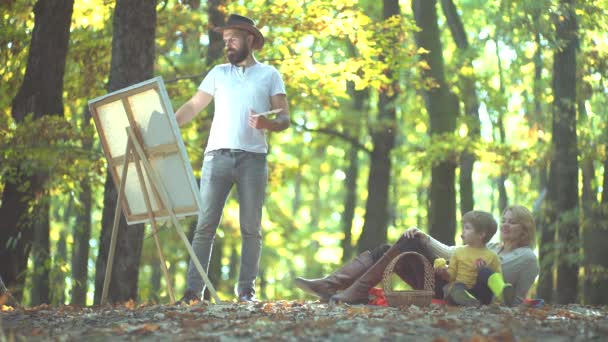 Чоловік художник малює картини на осінній природі. Щаслива мати батько і син в осінньому парку. Щаслива сім'я. Романтичне кохання . — стокове відео
