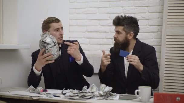Portret van twee jonge zakenmannen met Amerikanen bankbiljetten in een persoon en Bank kar in een ander, kiezen aarzelend. Zakenman overtuigt collega om bankkaart te gebruiken in ruil voor geld. — Stockvideo
