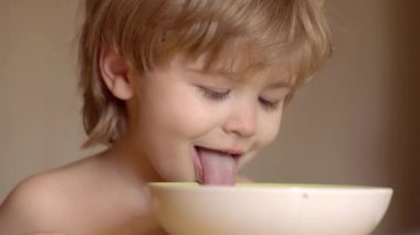 Genç çocuk yüzünde komik ifade ile sağlıklı yemek yemek masada oturuyor. Mutlu erkek bebek kaşık kendini yiyor. Bebek yeme.