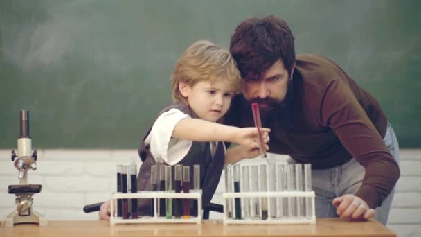 Père et fils. Un gamin de l'école primaire. Tutorat. C'était une petite expérience de chimie. Enseignant aider le jeune garçon avec la leçon. Joyeux dessin d'élève souriant au bureau. Cours de chimie scolaire . — Video