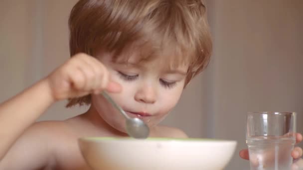 Niño sentado en la mesa comiendo comida saludable con expresión divertida en la cara. Comer niños. Un chico lindo está comiendo. Un niño desayunando en la cocina. Comida y bebida para niños . — Vídeos de Stock