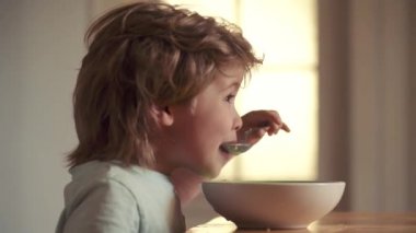 Mutfakta ki çocuk masada yemek yiyor. Neşeli bebek çocuk kaşıkla yemek kendisi yiyor. Çocuk yiyor. Çocuk bakımı. Sevimli çocuk yiyor. Mutlu çocuk kahvaltı var.