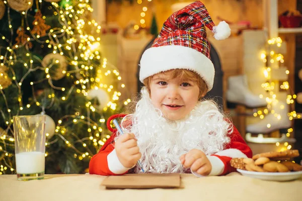 Portrait of Santa Claus writes the letter to children. Kid Santa Claus enjoying in served gingerbread cake and milk. — Stock Photo, Image