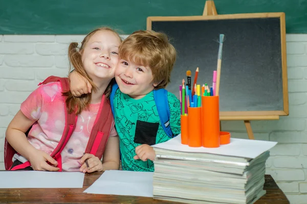 Возвращайся в школу. Девочка и мальчик со счастливым выражением лица возле стола со школьными принадлежностями . — стоковое фото