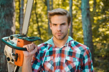 Erkek işi yapan adam. Oduncu ciddi bir yüz üzerinde testere taşır. Ormanların yok olması, doğal ekosistemlerin toprak bozulması ve istikrarsızlaşmasının önemli bir nedenidir..