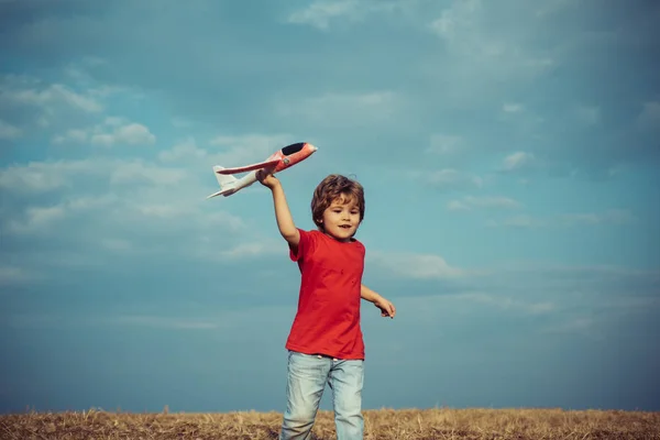 楽しさと笑顔を持って牧草地の上におもちゃの飛行機で遊ぶ子供。田舎の子供時代。ヴィンテージ色調の草原でおもちゃの飛行機で遊ぶかわいい子供. — ストック写真