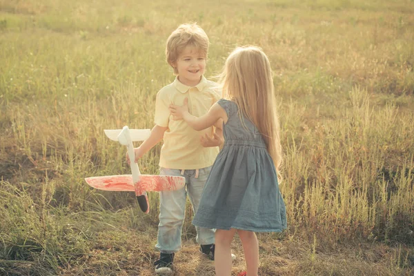ラブストーリー。楽しさと笑顔を持って牧草地の上におもちゃの飛行機で遊ぶ2人の幸せな子供の男の子と女の子。幸せな子供たち - 夏のフィールド上の姉妹と兄弟。冒険と休暇子供の概念. — ストック写真