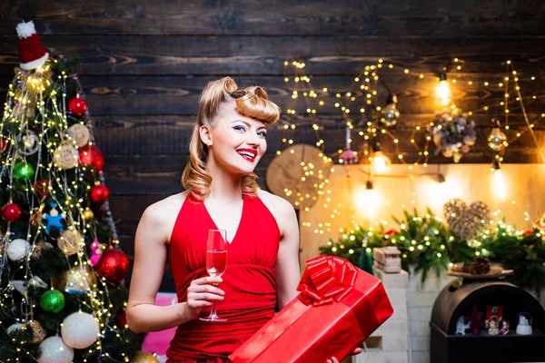 Retro pin-up vrouw poseren op Vintage houten kerst achtergrond. Vrolijk kerstfeest en gelukkig Nieuwjaar. Jonge vrouw in elegante rode jurk over Kerstmis interieur achtergrond. — Stockfoto